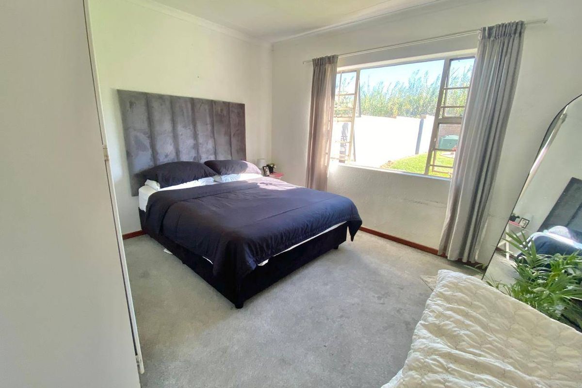 A bedroom featuring carpeted flooring, a built-in cupboard, and a large steel-framed window with views of the garden.