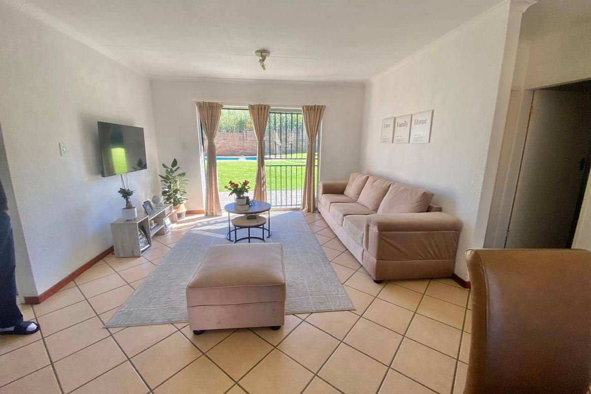 A bright living room featuring tiled flooring and a sliding glass door that provides direct access to the outdoor patio and garden area.