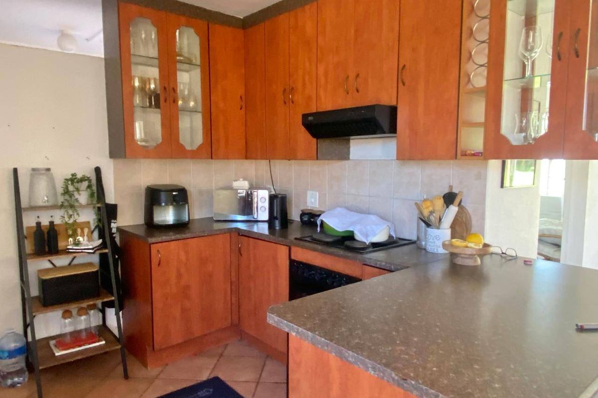 A functional kitchen featuring wood-finish cabinetry, dark countertops, a built-in hob and oven, and tiled flooring, offering a classic layout with ample storage space.