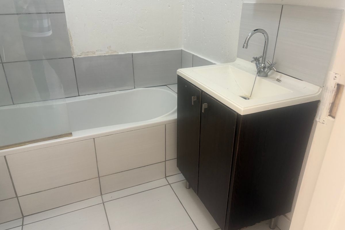 A compact bathroom featuring a bathtub with a glass screen, tiled walls, and a dark wood vanity cabinet with a basin.
