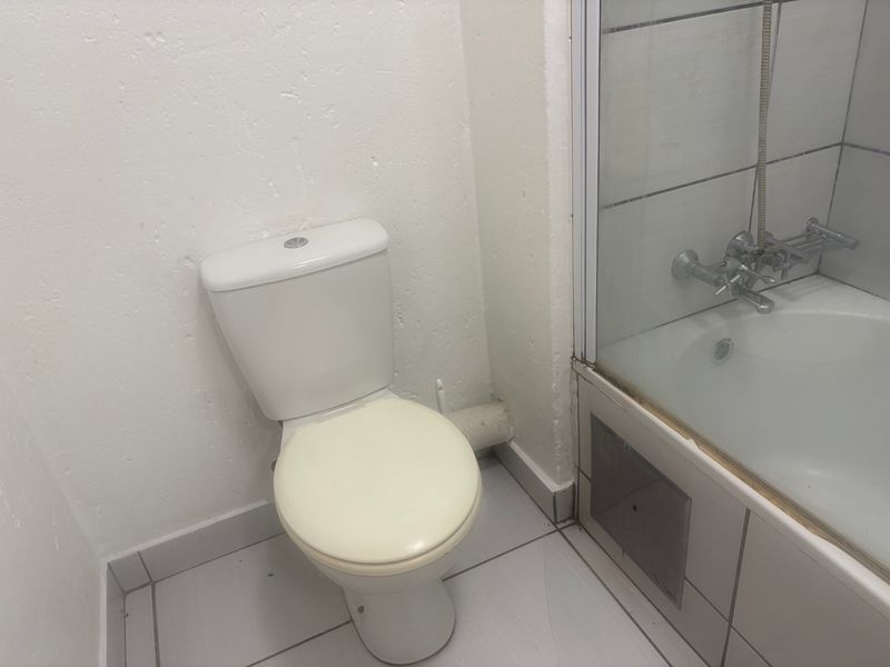 A functional bathroom featuring a standard toilet and a bathtub with a shower mixer, finished with tiled flooring and wall surrounds.