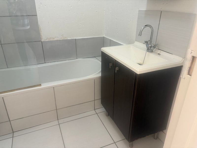 A compact bathroom featuring a bathtub with a glass screen, a vanity basin, and neutral wall and floor tiling.