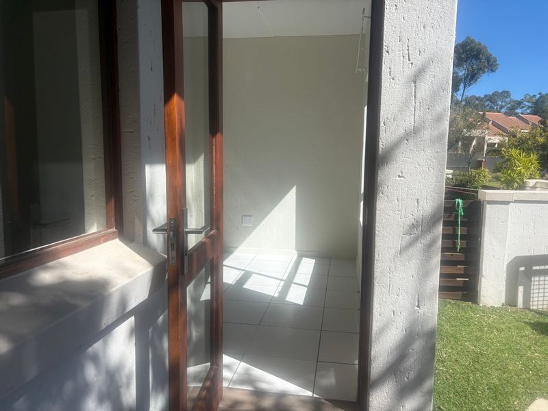 A covered patio area featuring tiled flooring and a timber-framed glass door, providing direct access to the outdoor garden space.