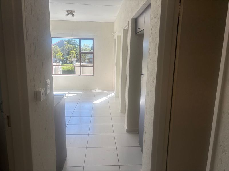 A bright, empty hallway featuring tiled flooring, built-in storage cupboards, and natural light streaming through a large window.