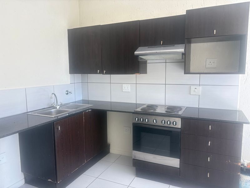 A functional kitchen featuring dark wood cabinetry, granite countertops, a built-in oven with hob, and a stainless steel sink with tiled splashback.