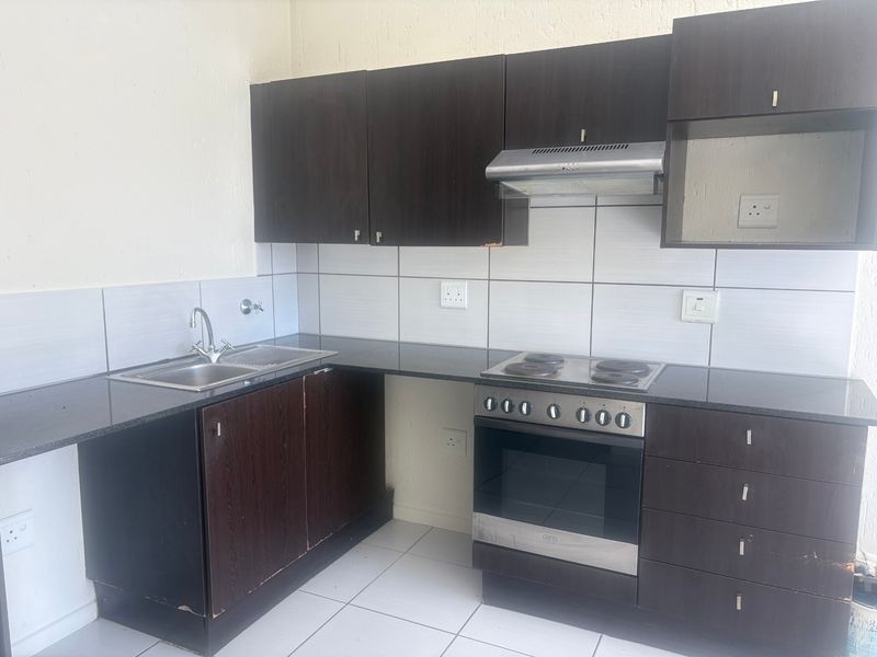 A functional kitchen featuring dark wood cabinetry, granite countertops, a built-in oven with hob, and a stainless steel sink with tiled backsplash.