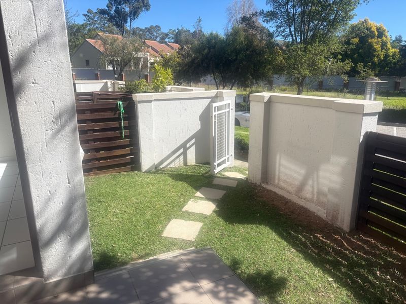 A private rear garden area featuring a paved path, lawn, timber privacy screening, and a secure pedestrian gate set within a boundary wall.