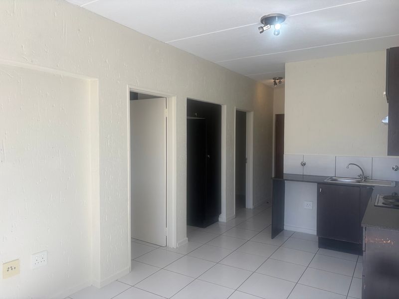 An open-plan living and kitchen area featuring tiled flooring, built-in kitchen cabinetry with a sink and hob, and access to multiple rooms.