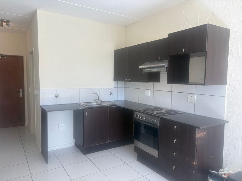 A functional kitchen featuring dark wood cabinetry, granite countertops, a built-in electric stove with extractor fan, and tiled flooring.