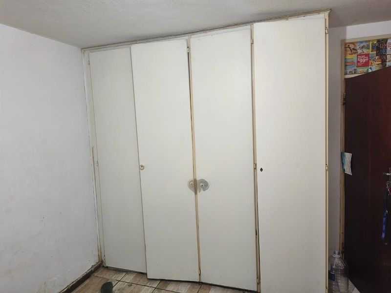 A bedroom featuring built-in cupboards and tiled flooring, currently vacant and in need of cosmetic updates to improve its overall condition.