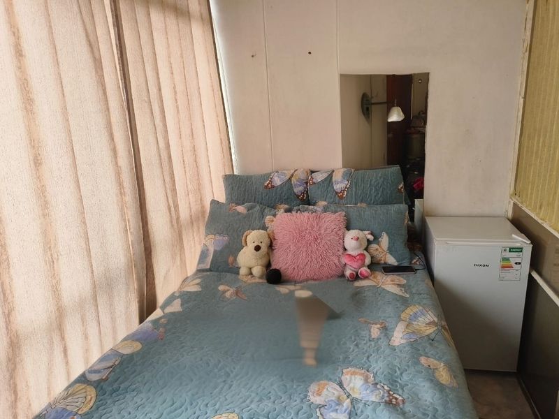 A compact bedroom featuring a built-in mirror and wall surface wear, requiring cosmetic updates to improve the overall aesthetic and condition.