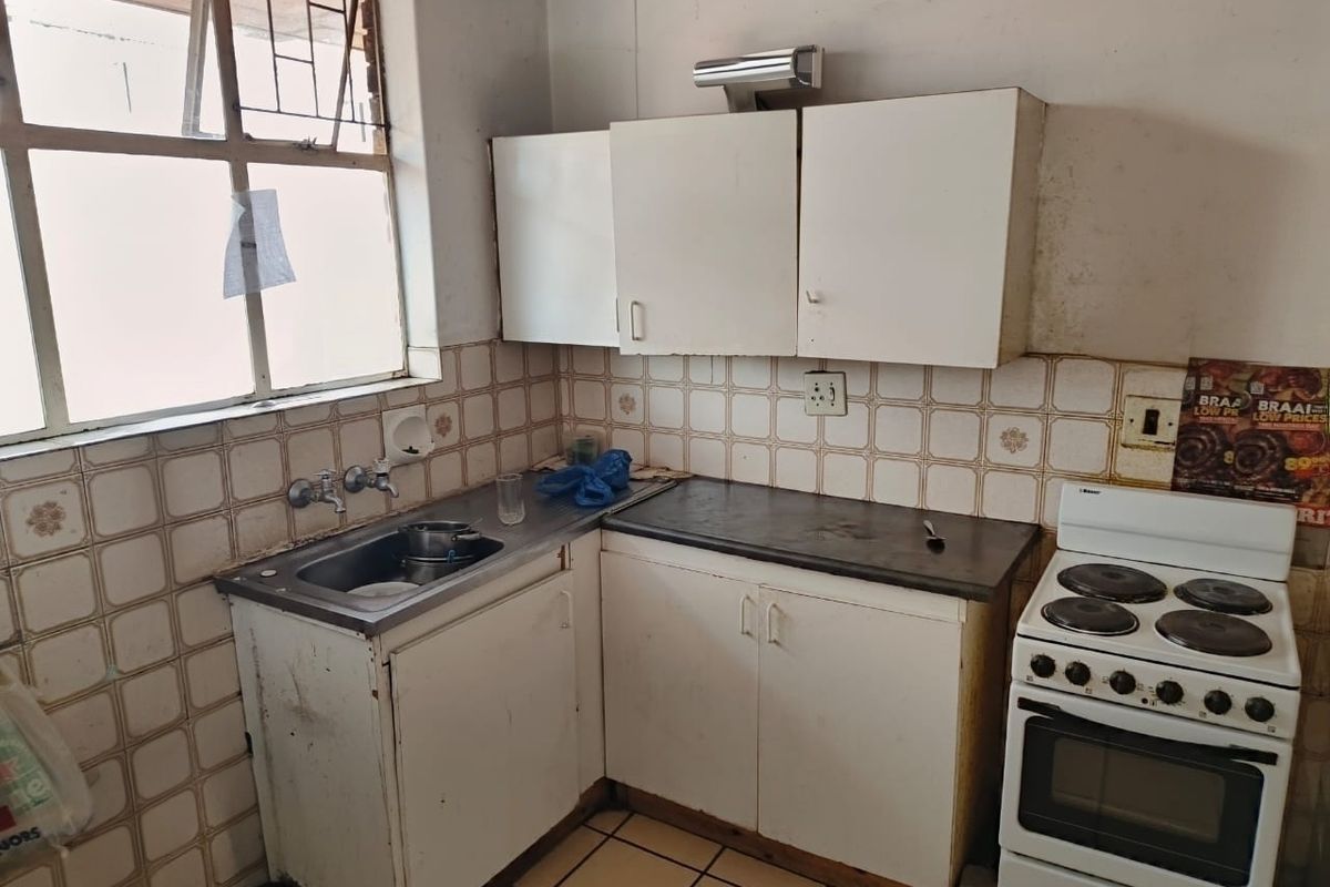 A dated kitchen featuring original cabinetry, tiled splashbacks, and a freestanding electric stove, offering significant potential for modernization and renovation.