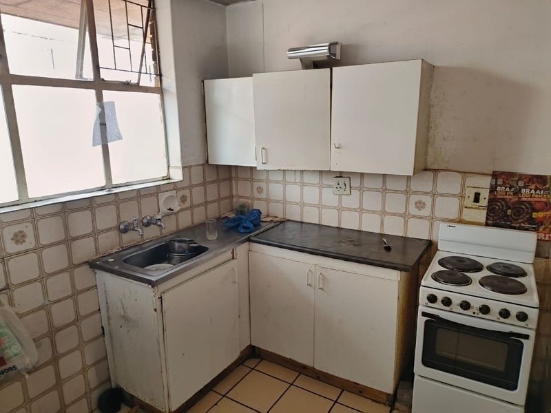 A dated kitchen featuring original cabinetry, tiled splashbacks, and a freestanding electric stove, offering significant potential for modernization and renovation.