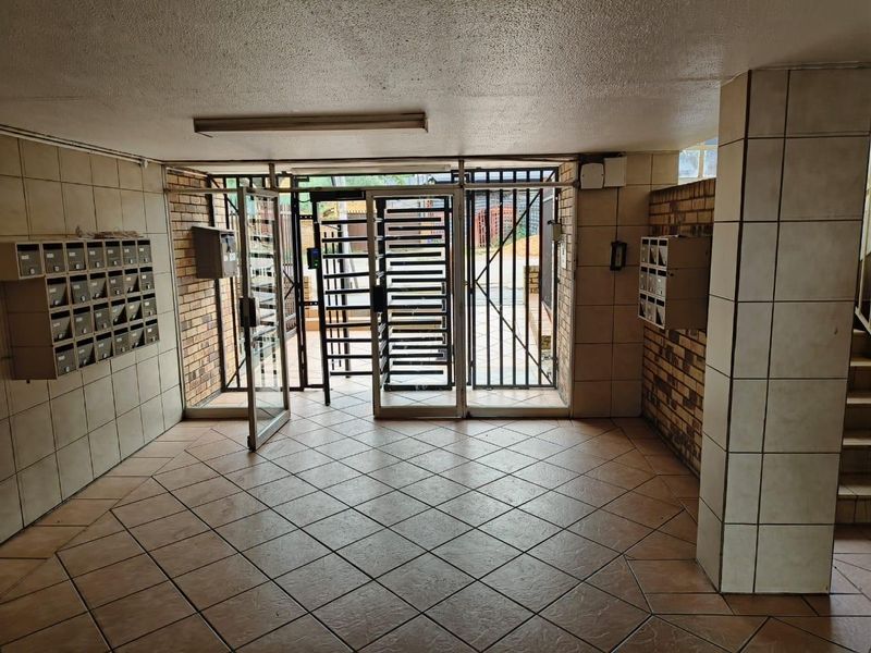 A secure apartment building entrance lobby featuring tiled flooring, brick wall accents, and integrated metal mailboxes for residents.