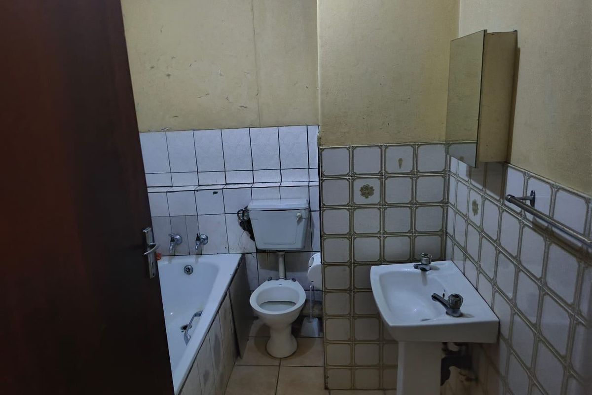 A dated bathroom featuring a standard bathtub, pedestal basin, and toilet with original wall tiling, requiring modernization and cosmetic updates.