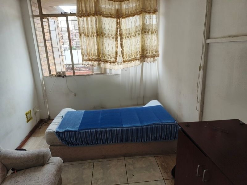 A bedroom featuring tiled flooring and a large window, currently requiring cosmetic updates and wall repairs to improve its overall condition.