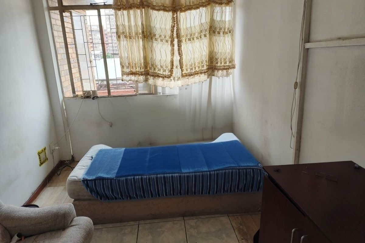 A bedroom featuring tiled flooring and a large window, currently requiring cosmetic updates and wall repairs to improve its overall condition.