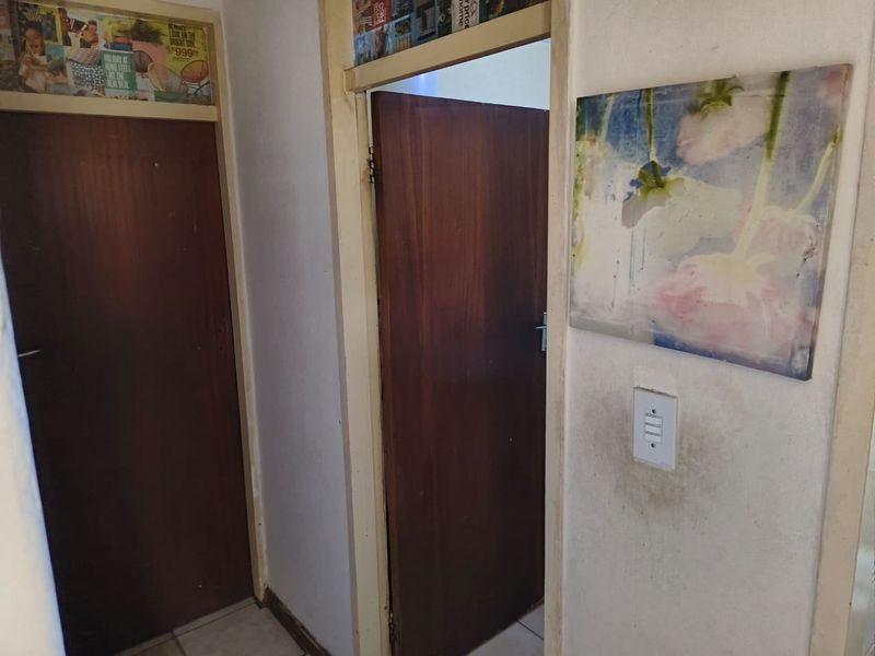 A narrow interior hallway featuring wooden doors and frames, showing signs of wear and wall staining requiring maintenance.