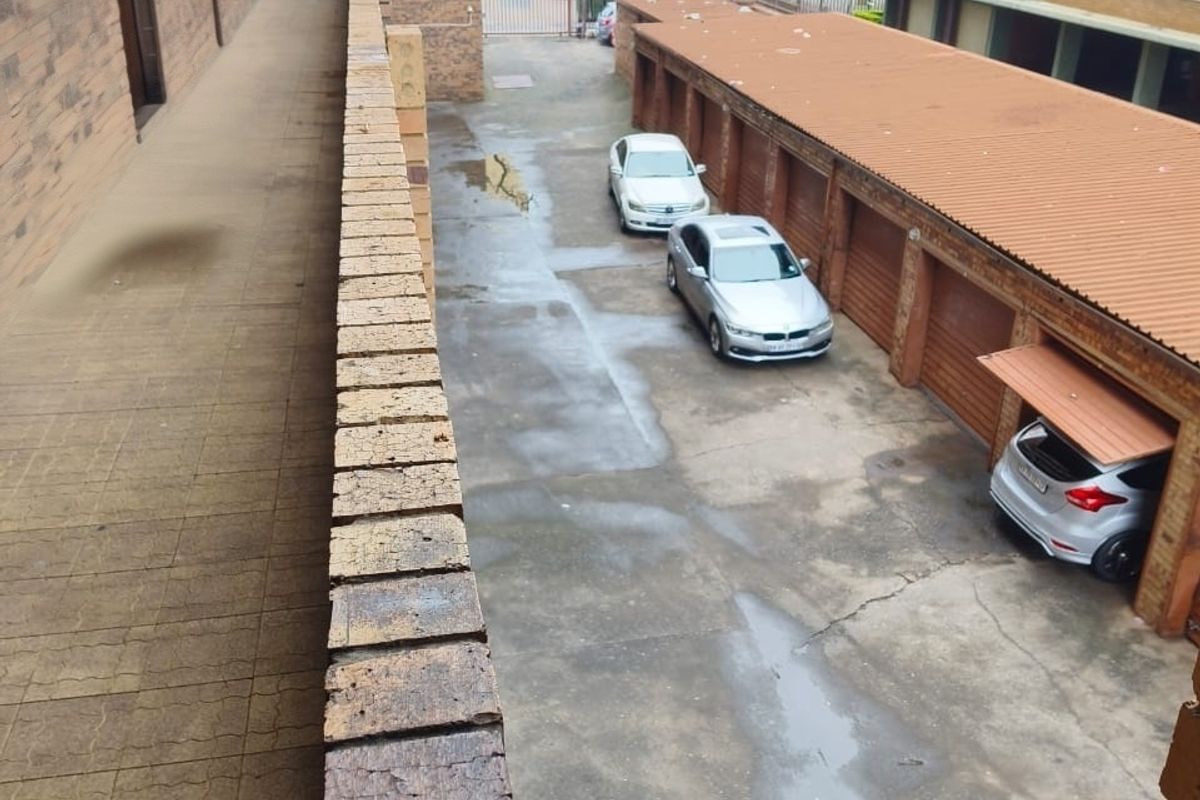 An elevated view of the apartment complex exterior, featuring a brick walkway, communal driveway, and a row of garages with corrugated roofing.