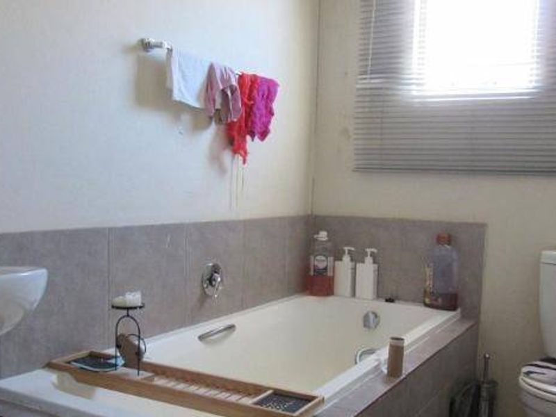 A functional bathroom featuring a built-in bathtub, pedestal basin, and toilet with neutral wall tiling.