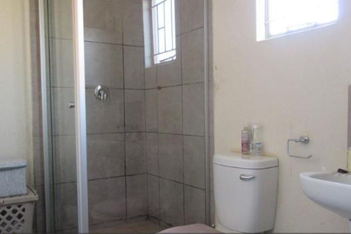 A functional bathroom featuring a shower enclosure, pedestal basin, and toilet, with neutral wall finishes and security bars on the window.