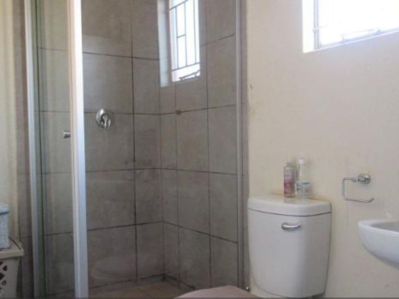 A functional bathroom featuring a shower enclosure, pedestal basin, and toilet, with neutral wall finishes and security bars on the window.