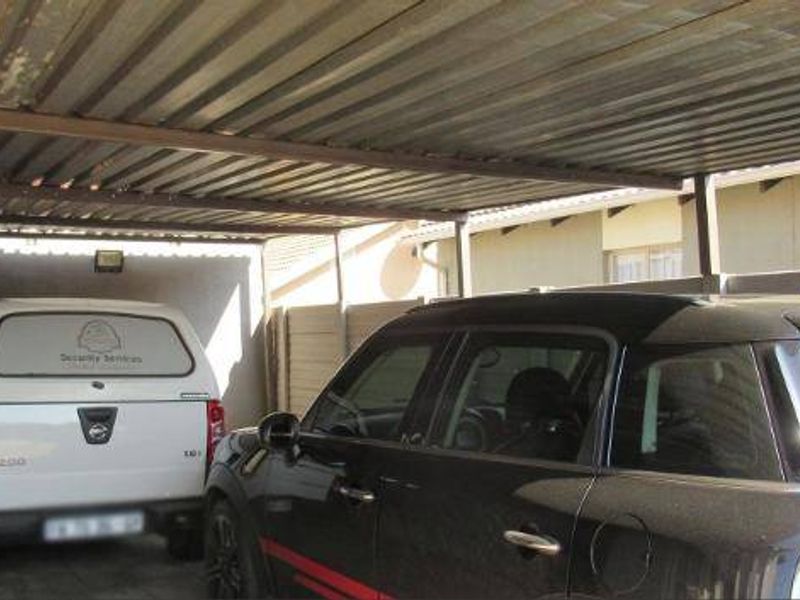 A covered carport area featuring a corrugated metal roof structure and precast concrete perimeter walling.