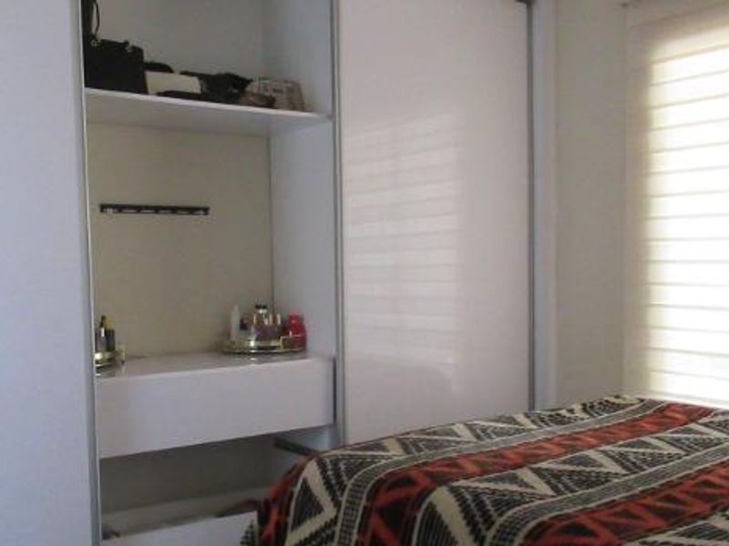 A bedroom featuring a built-in wardrobe with integrated shelving and modern roller blinds for light control.