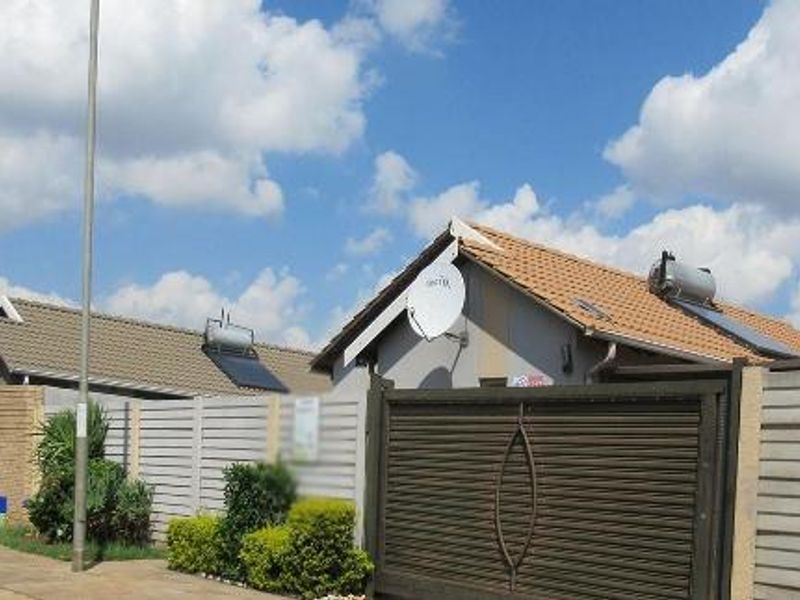 Front view of a residential property featuring a tiled roof with solar water heating, secure precast boundary walls, and a metal sliding gate.