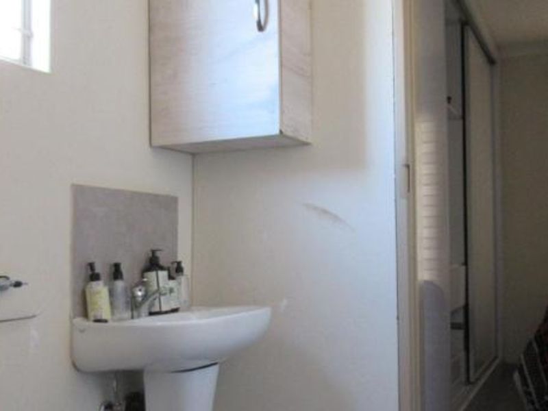 A compact bathroom area featuring a pedestal basin and wall-mounted storage cabinet, adjacent to a bedroom with built-in sliding door wardrobes.