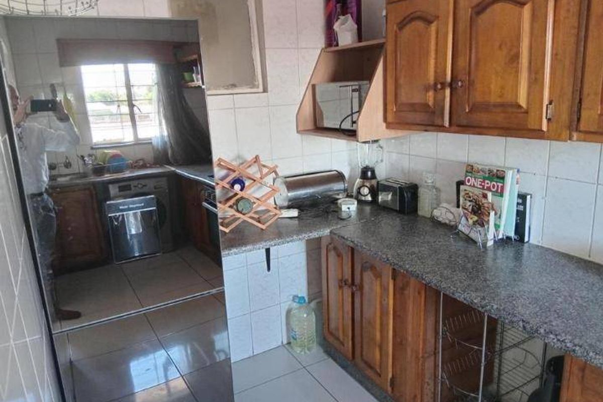 A dated kitchen featuring wooden cabinetry, granite countertops, and tiled finishes, offering a functional layout with potential for modern renovation.