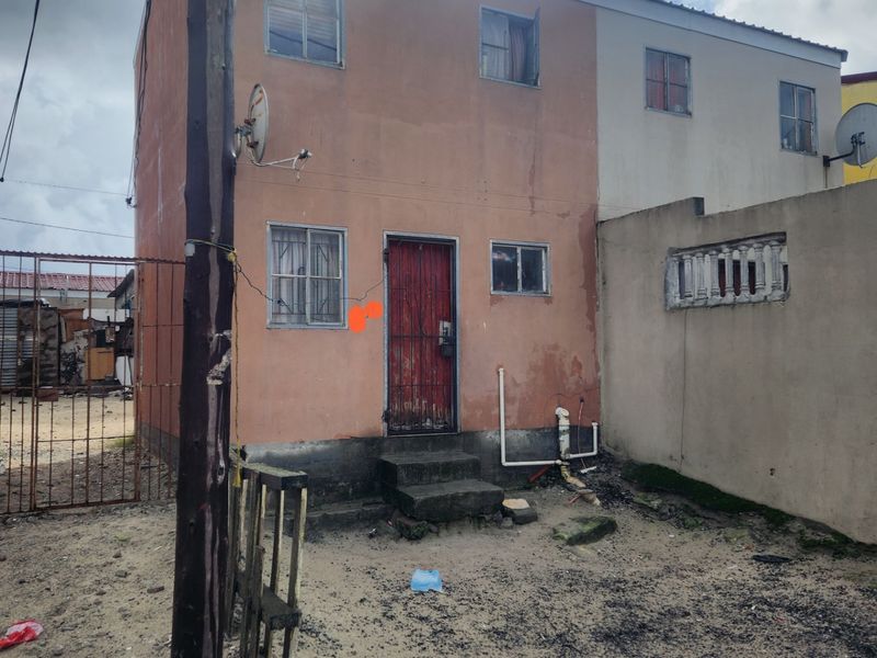 Front exterior view of a two-story apartment building featuring a security gate, security bars on windows, and an unpaved yard area.