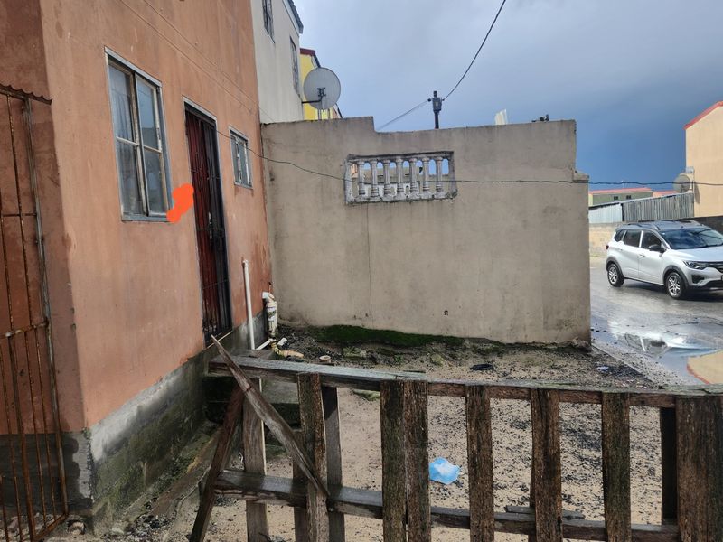 Exterior view of the apartment building facade showing a security gate, metal window frames, and a weathered boundary wall with visible signs of wear.
