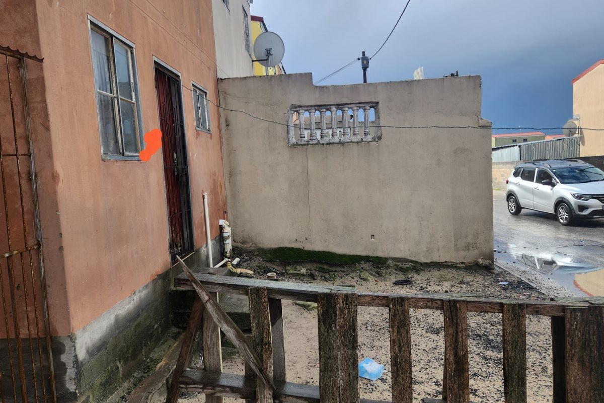 Exterior view of the apartment building facade showing a security gate, metal window frames, and a weathered boundary wall with visible signs of wear.