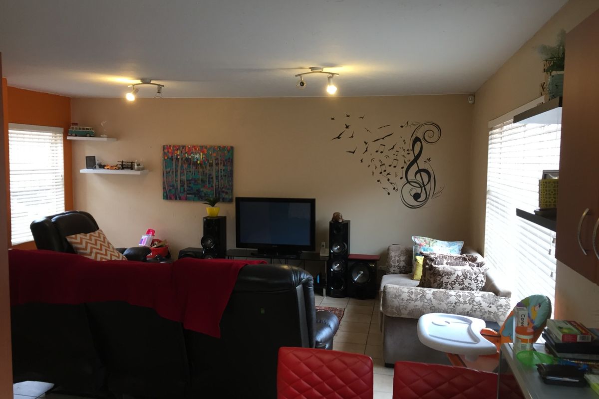 A living room area featuring tiled flooring, track lighting, and large windows with venetian blinds, offering a functional and comfortable space.