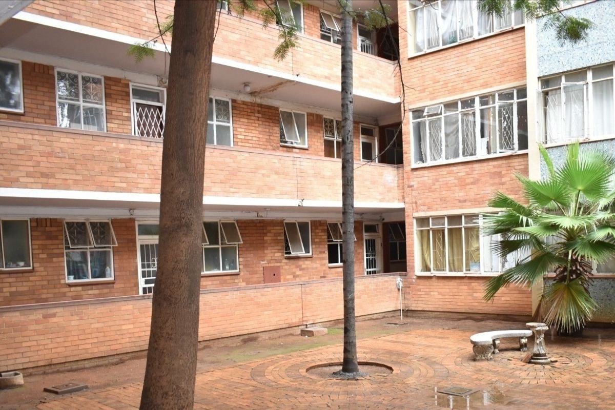 A view of the apartment complex courtyard featuring exposed brick facades, multi-level walkways, and a paved central area with established trees.