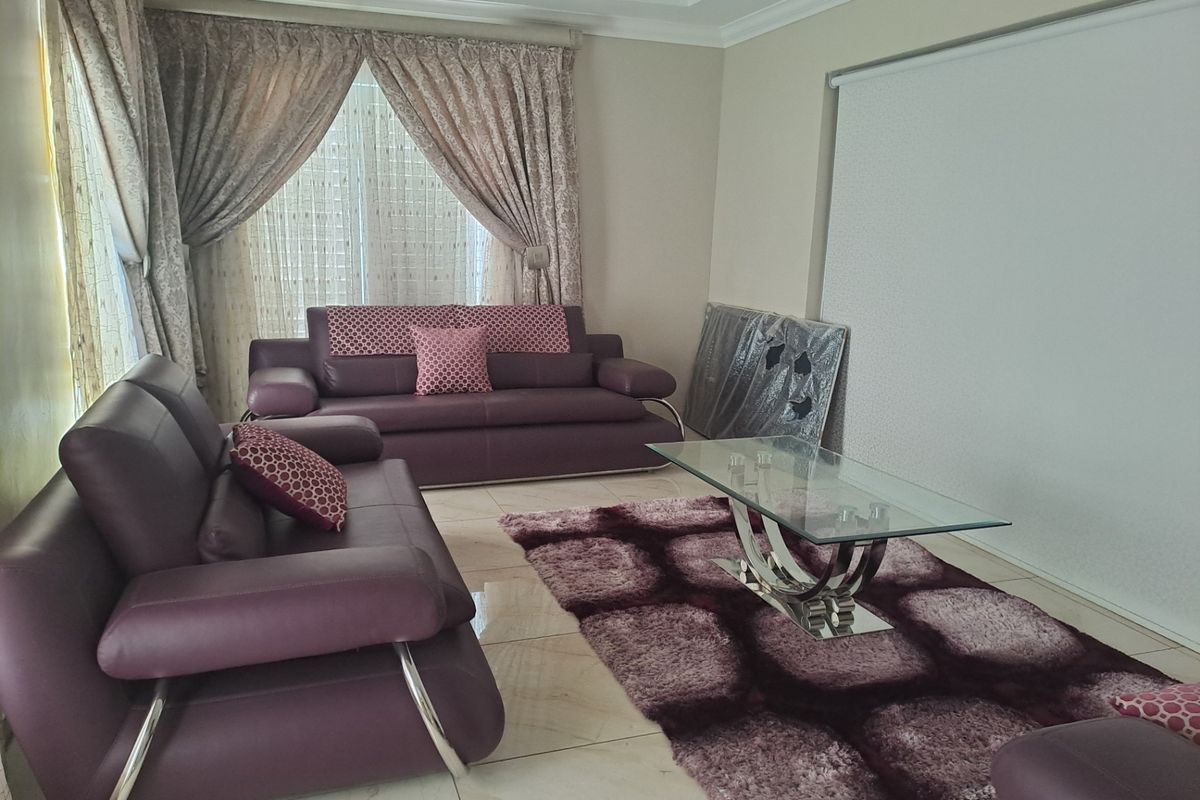 A well-maintained living room featuring polished floor tiles, decorative ceiling cornices, and large windows with layered curtain treatments.