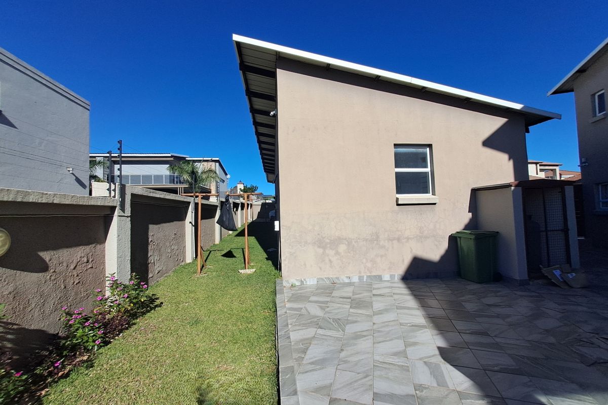 A side exterior view of the property featuring a paved patio area, a narrow lawn, and a perimeter boundary wall.
