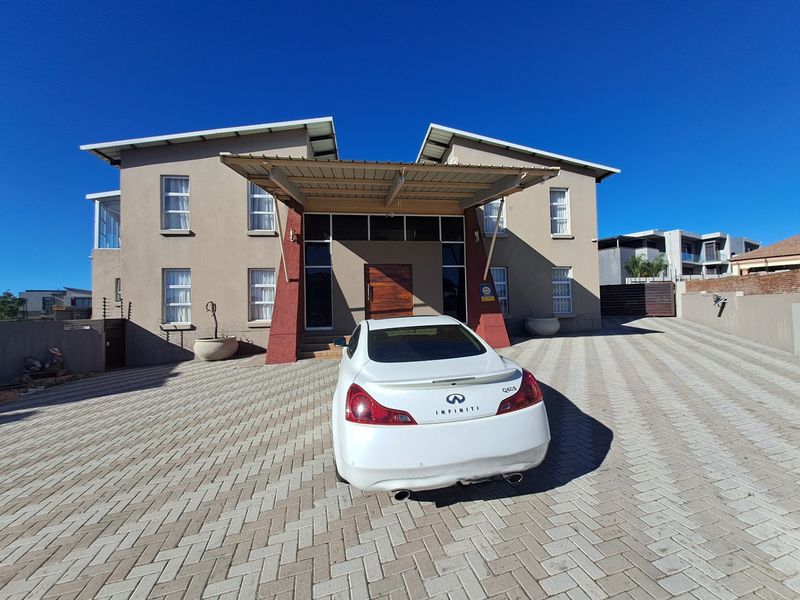Front elevation of a modern double-story house featuring a paved driveway, covered entrance portico, and secure perimeter fencing.