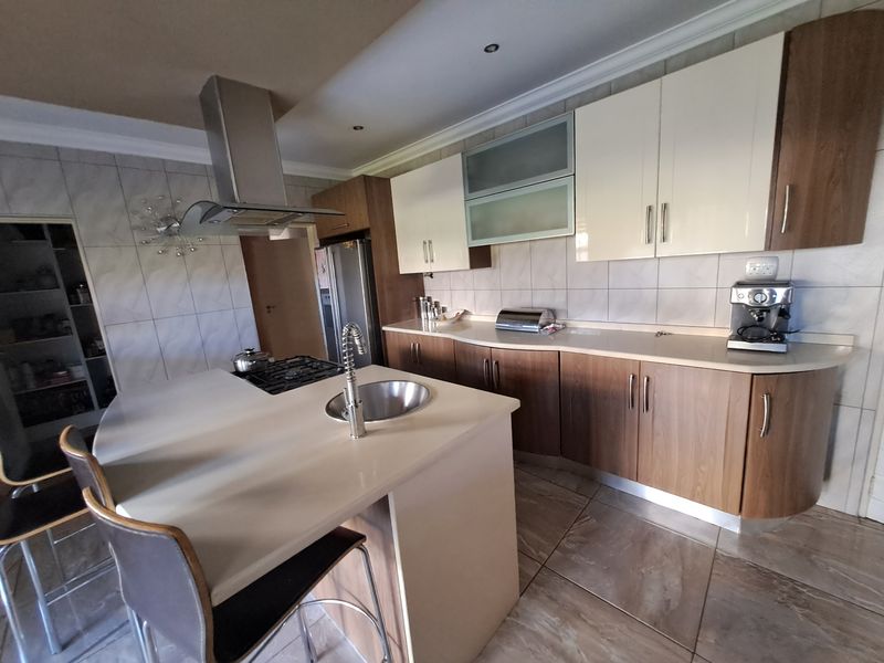 Modern kitchen featuring a central island with a gas hob, ample built-in cabinetry, tiled flooring, and a dedicated pantry area.