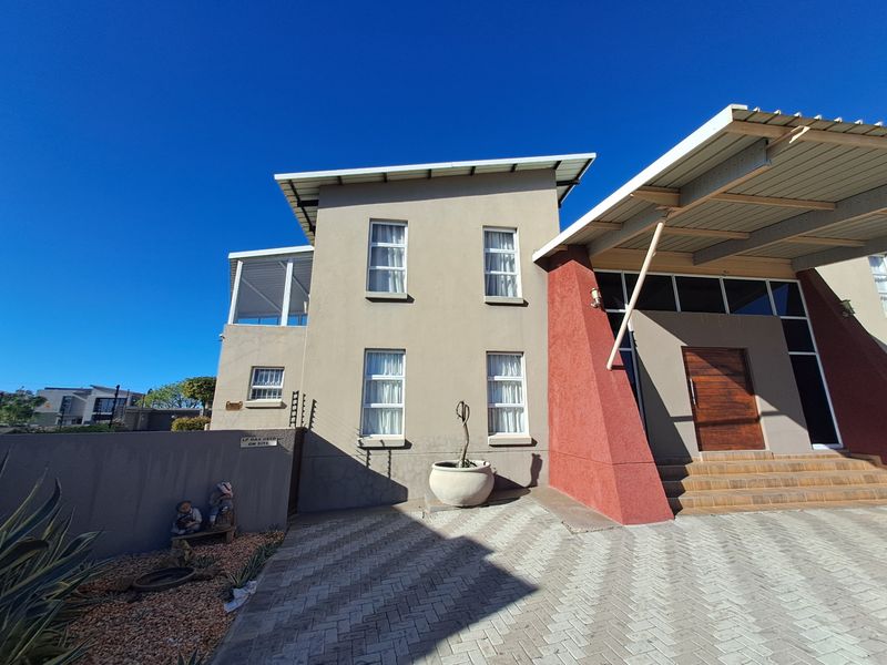 Front elevation of a modern two-story house featuring a paved driveway, covered entrance with timber door, and secure perimeter fencing.