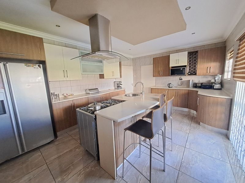 Modern kitchen featuring a central island with gas cooktop, stainless steel extractor fan, stone countertops, and ample built-in cabinetry with tiled flooring.