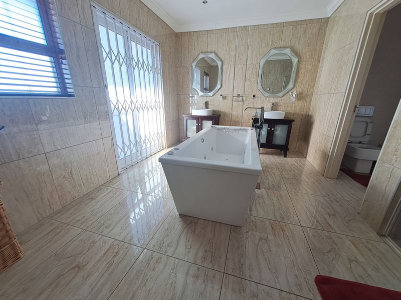 Spacious modern bathroom featuring a central freestanding bathtub, double vanity with vessel sinks, and floor-to-ceiling neutral tiling.
