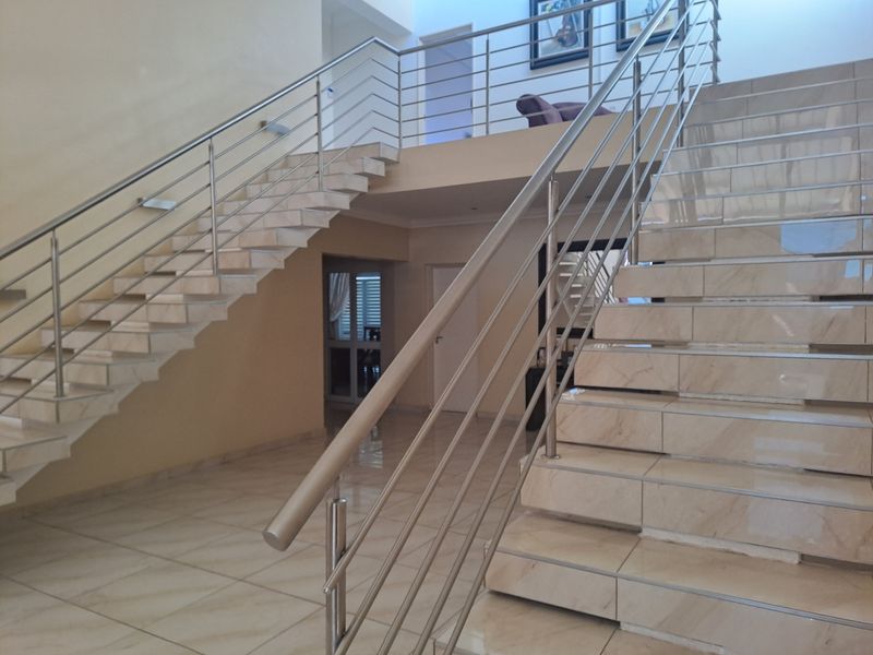 Spacious entrance hall featuring a grand tiled staircase with a modern stainless steel balustrade leading to an upper mezzanine level.