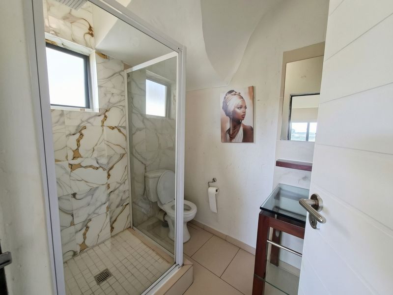 A modern bathroom featuring a glass-enclosed shower with marble-patterned wall tiles, a toilet, and a vanity basin with a wall-mounted mirror.