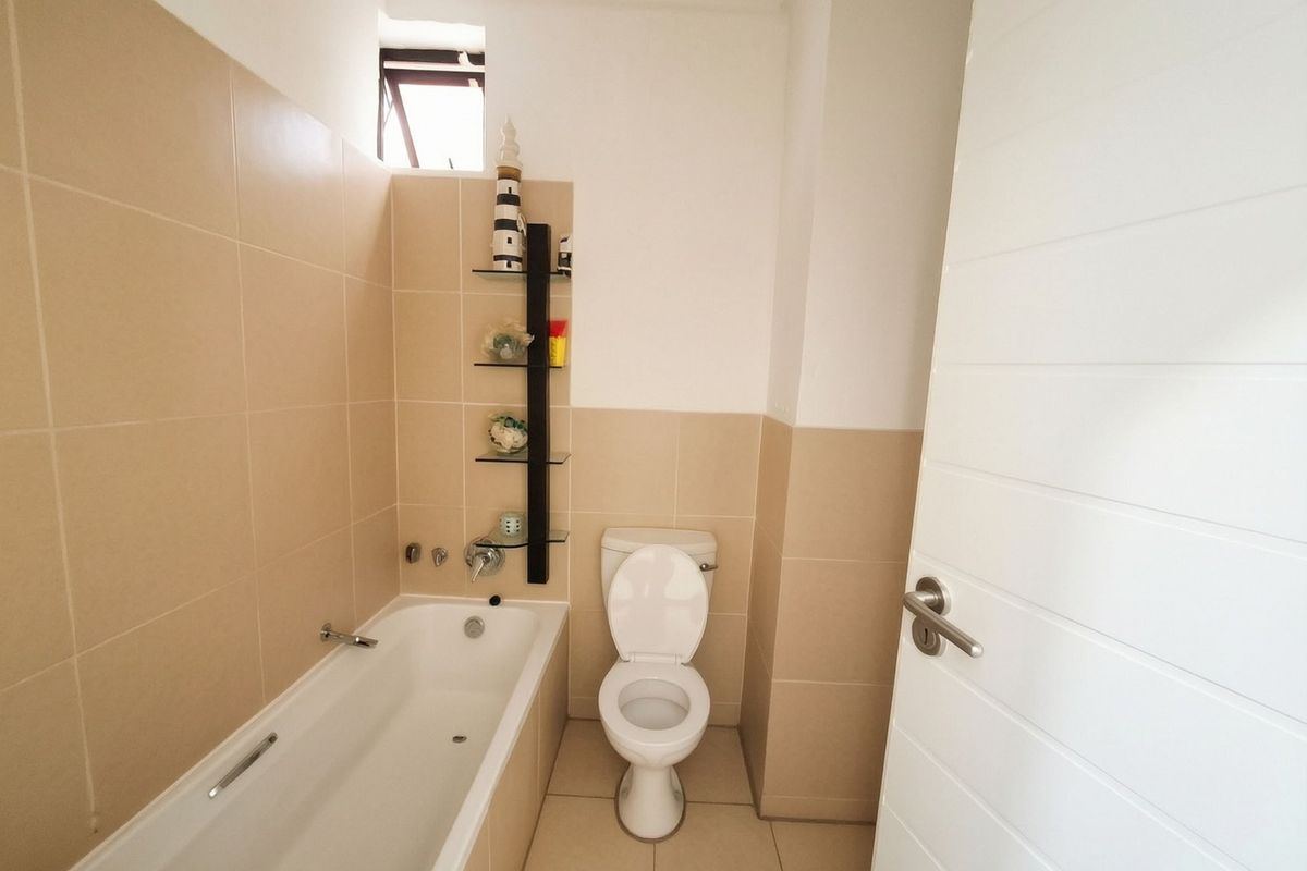 A clean, functional bathroom featuring a bathtub, toilet, and neutral wall tiling with built-in shelving.