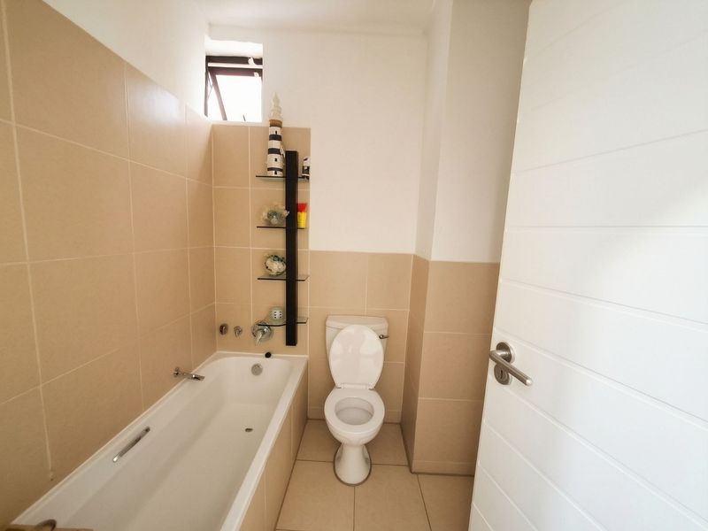 A clean, functional bathroom featuring a bathtub, toilet, and neutral wall tiling with built-in shelving.