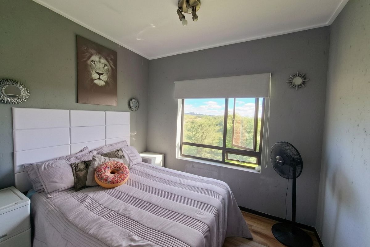 A bedroom featuring laminate flooring, a roller blind, and a ceiling light fixture, with views of the surrounding landscape.