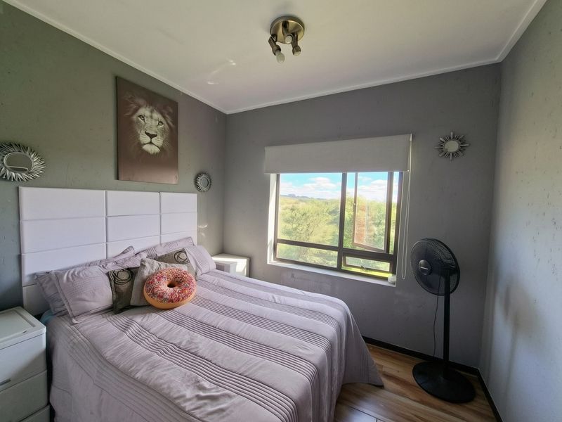 A bedroom featuring laminate flooring, a roller blind, and a ceiling light fixture, with views of the surrounding landscape.