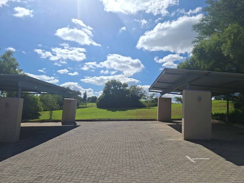 Open-air covered parking bays featuring paved surfaces, sturdy masonry pillars, and metal roofing, set within a well-maintained landscaped environment.